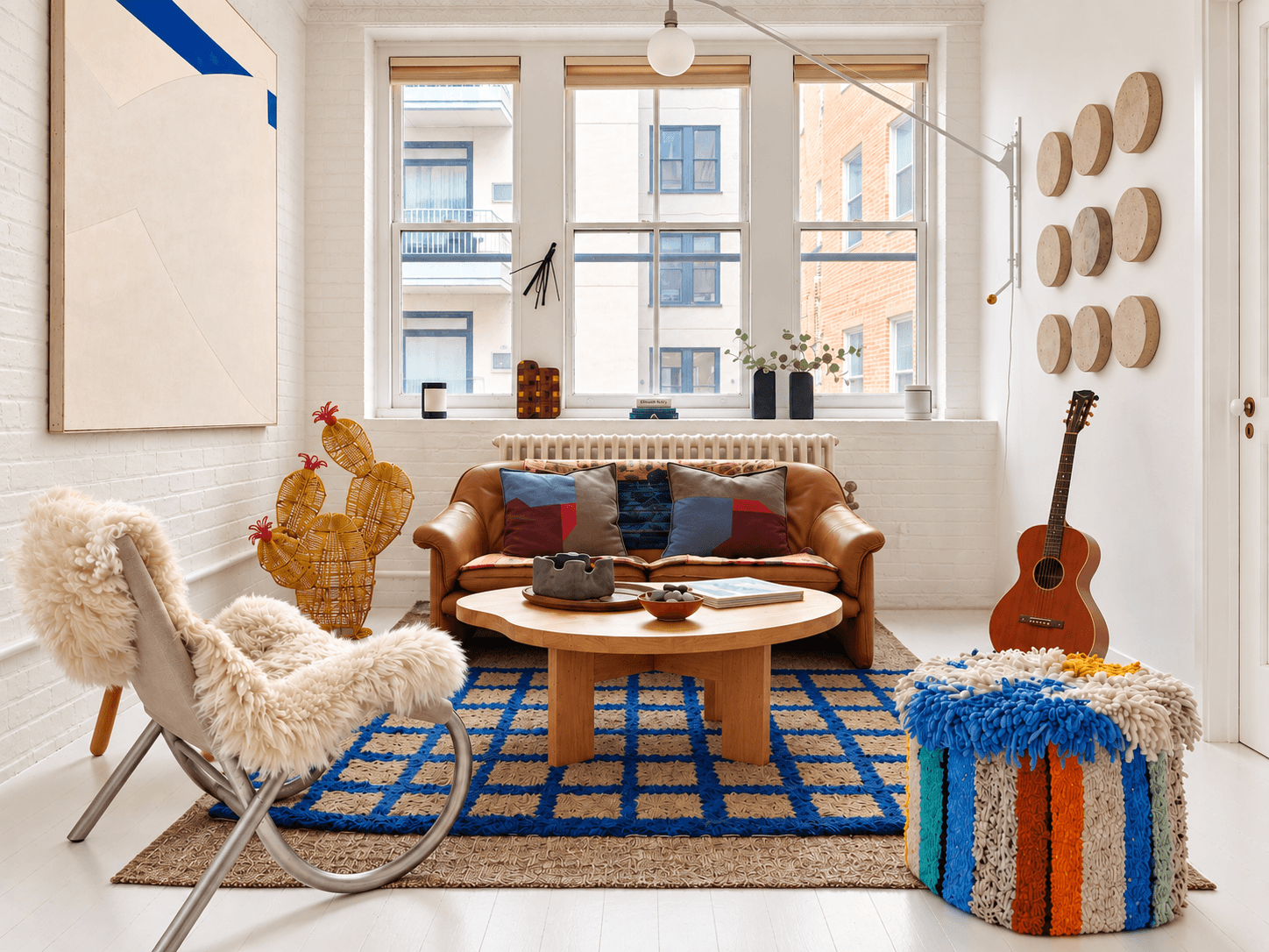 Loft living room with a cognac leather sofa, blue checked rug and three tall windows