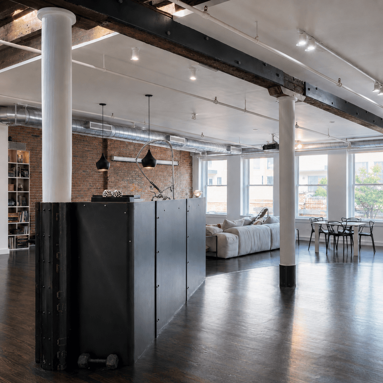 Open loft with white columns, exposed timber beams and a black steel partition, a sofa and windows beyond